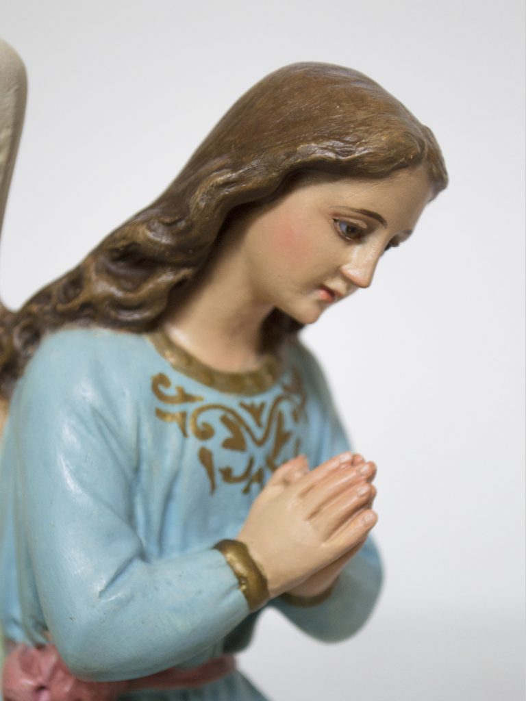 Detalle de una escultura policromada que representa un ángel con ropa azul en actitud de rezar.