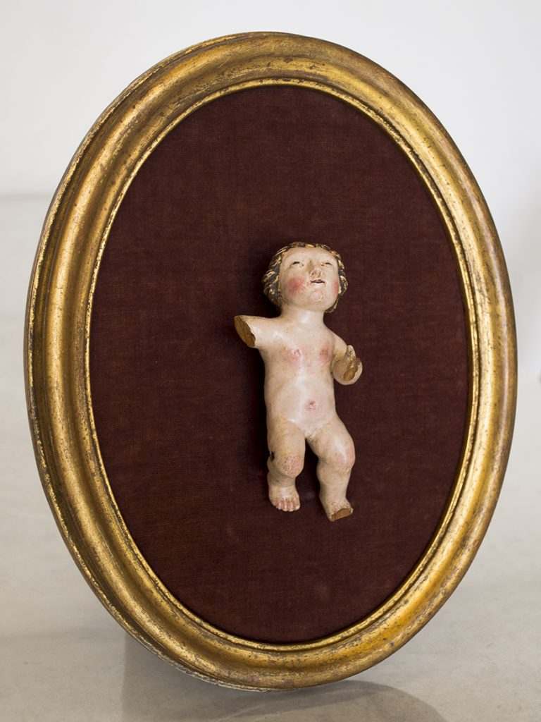 Escultura policromada de un niño tras su limpieza, sobre un marco dorado oval.